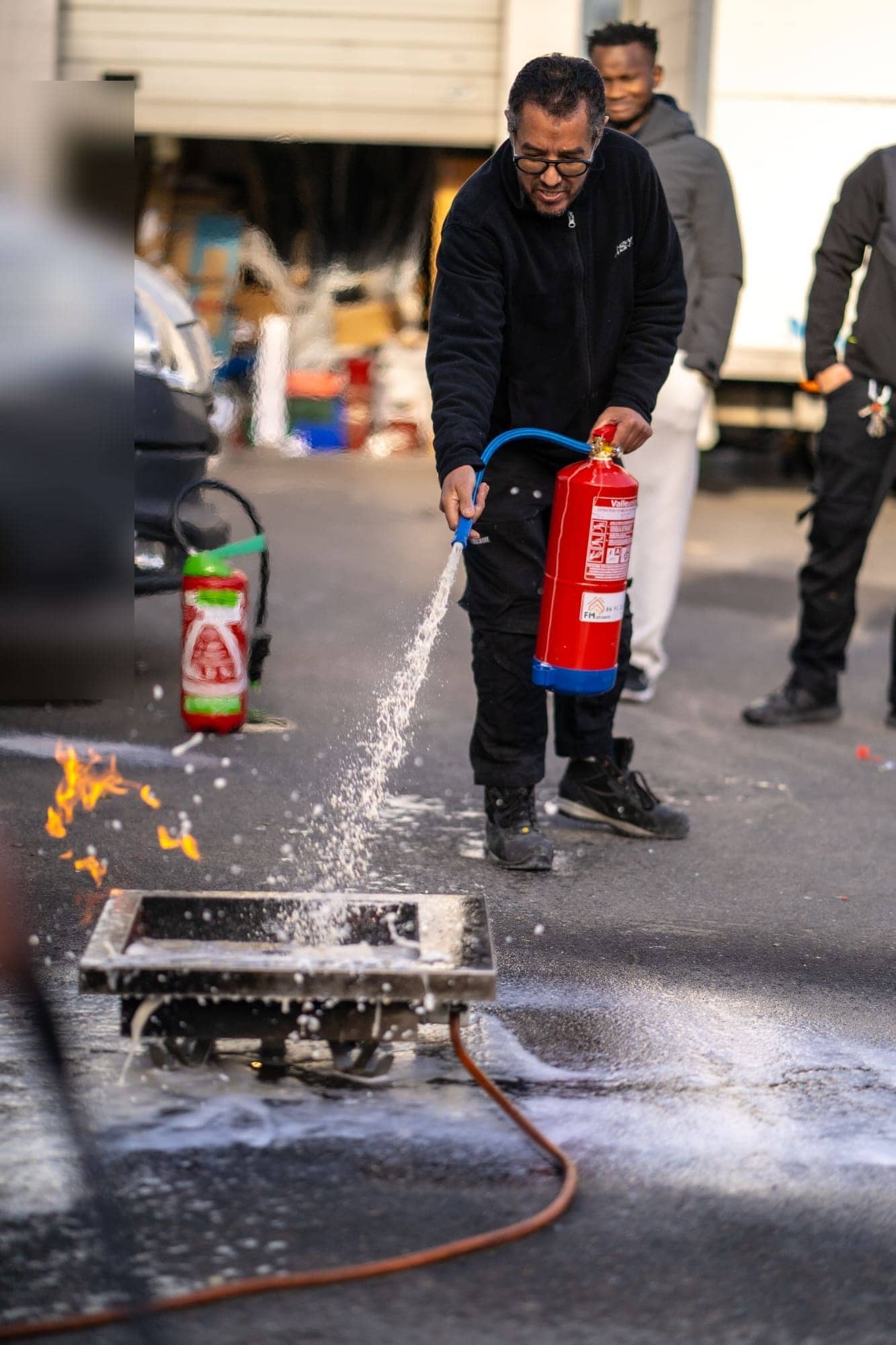 Stagiaire projetant l'agent extincteur à la base des flammes d'un bac à feu