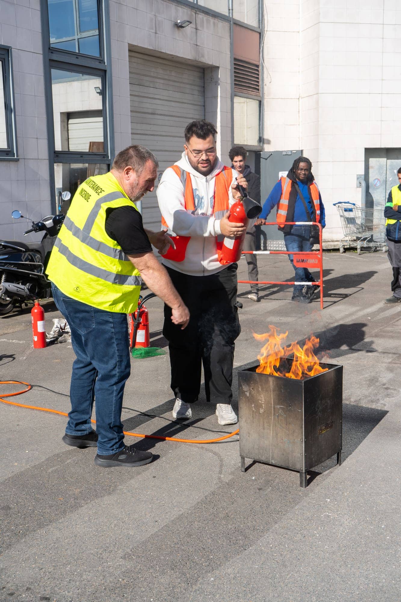 Formateur guidant un stagiaire pour percuter l'extincteur avant l'attaque du feu