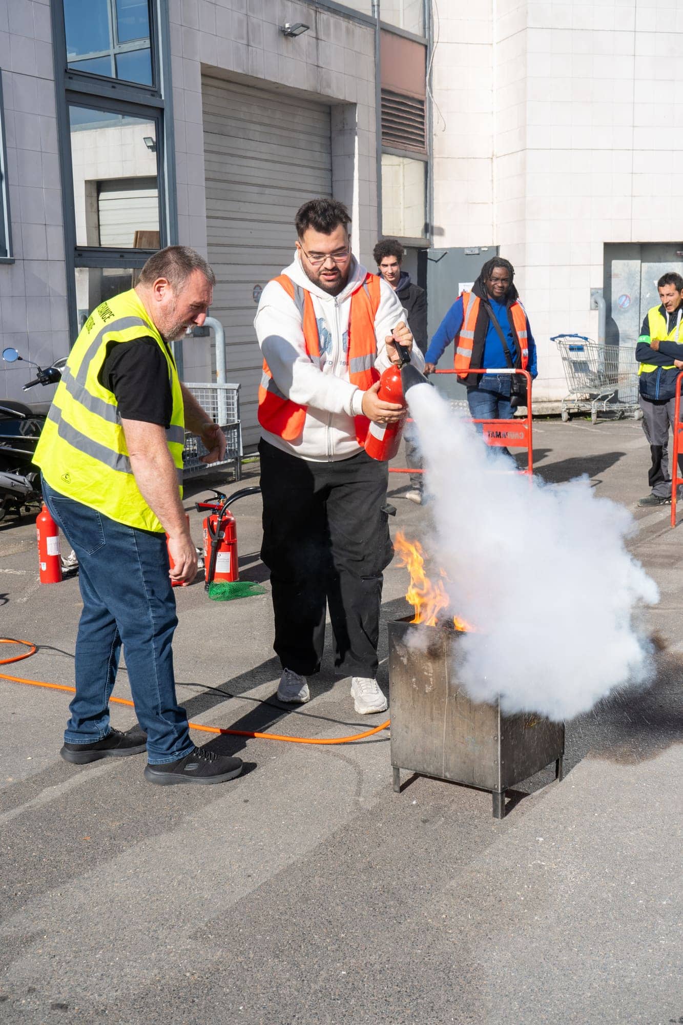 Stagiaire manipulant un extincteur sous le contrôle du formateur, exercice sur feu réel